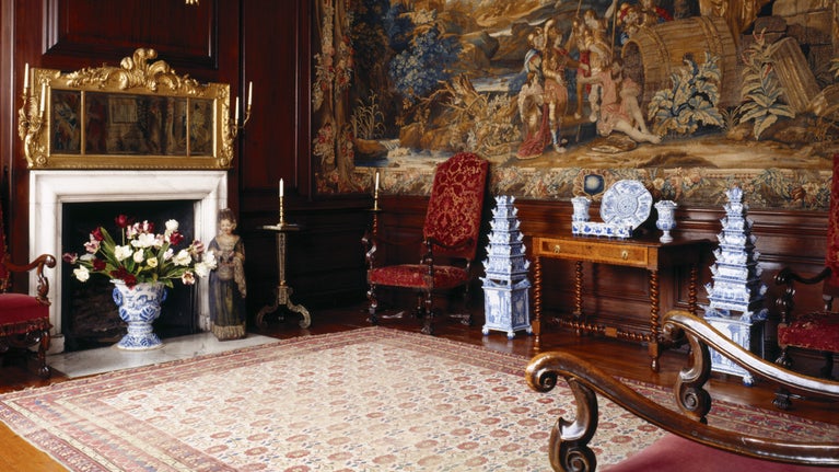The interior of the Diogenes Room at Dyrham Park, Bath, showing rich tapestries and Delftware, including two flower pyramid vases.